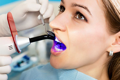 A woman receiving dental care with a device that appears to be a dental laser or machine.