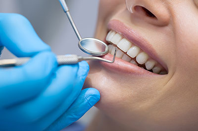 The image shows a dental professional performing a dental procedure on a patient s teeth using specialized tools, with the patient wearing a mouthguard and having their teeth cleaned.