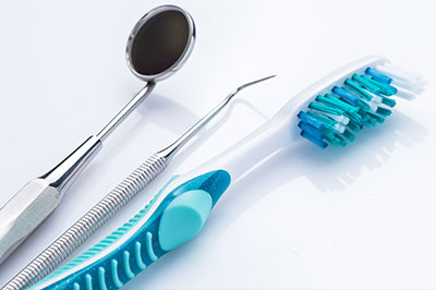 The image shows a collection of dental tools, including a toothbrush with blue bristles, a dental mirror, a pair of scissors with silver handles, and a small suction cup, all arranged on a white surface.