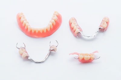 The image displays a collection of dental appliances, including braces, retainers, and possibly a partial denture, all with a pinkish-red hue, arranged on a white background.