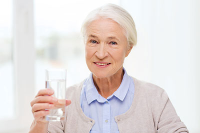 An elderly woman holding a glass of water with a smile on her face.