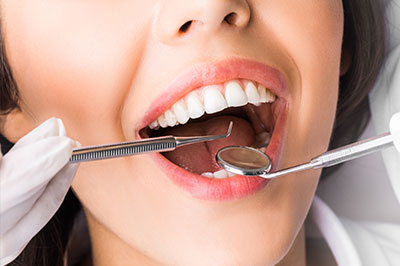 The image features a woman with an open mouth, receiving dental care from a professional using specialized equipment.