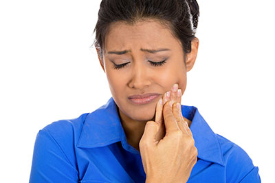 A woman with dark hair is looking upwards with her mouth open while holding an object near her teeth.