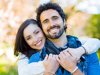 A man and woman are embracing each other in a joyful pose, both smiling and looking at the camera.