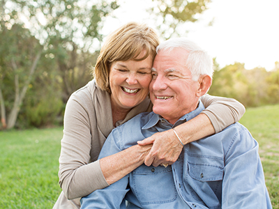 An elderly couple embracing each other outdoors during daylight hours.