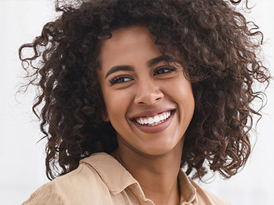 The image shows a person with curly hair smiling at the camera, wearing a light-colored top.